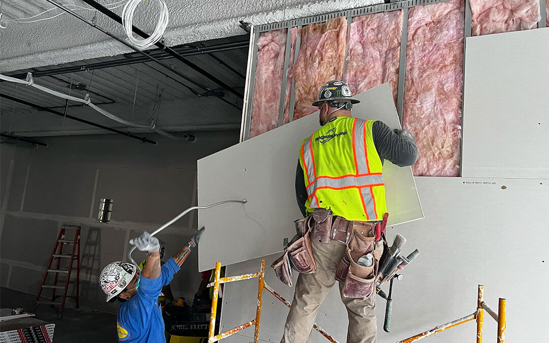 Two professional drywall contractors installing drywall on a job site.